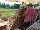 Jerry uses a template to guide the angle of the gable while Rob lays brick.